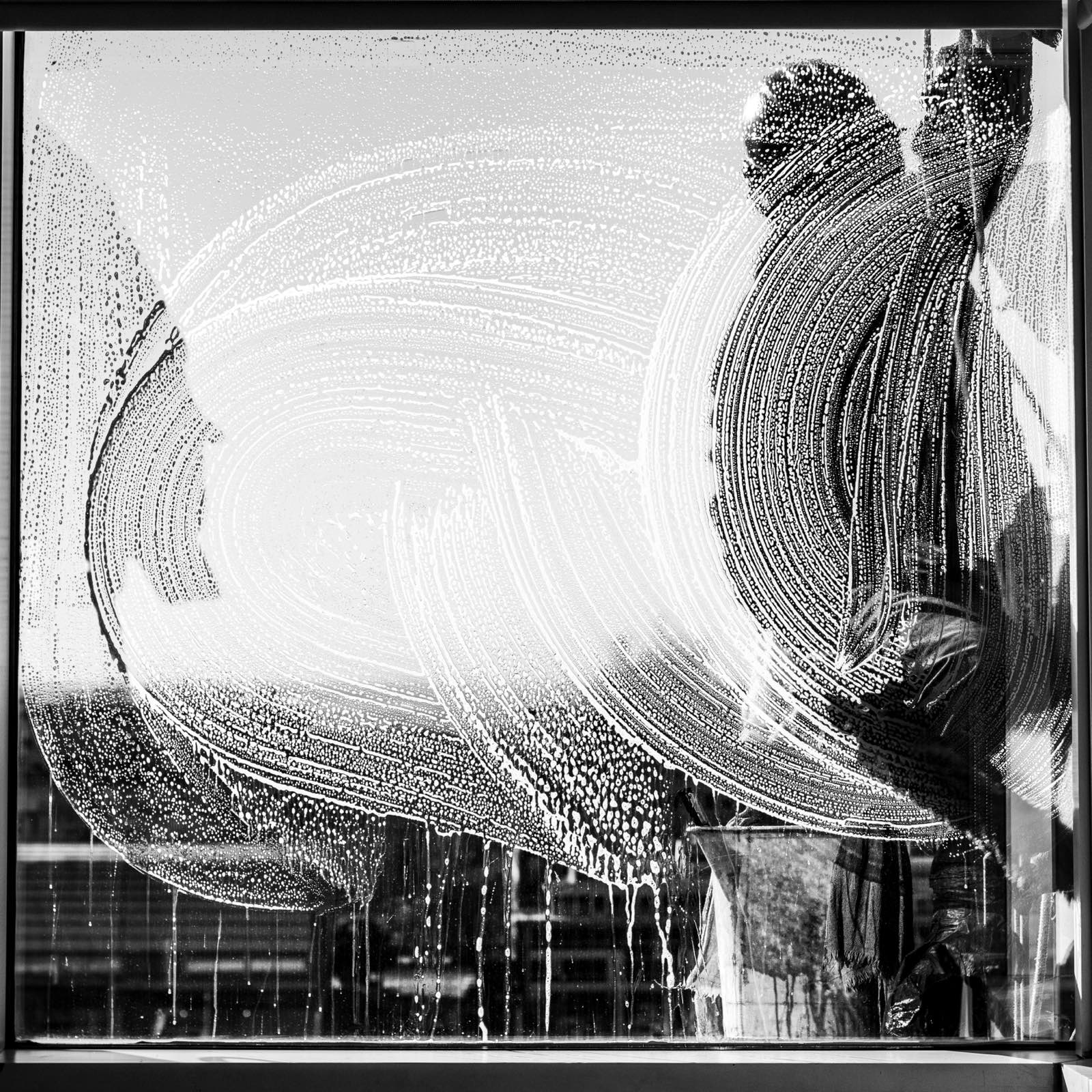 Solution swept in broad arcs across a pane of glass during application, seen from inside the building.
