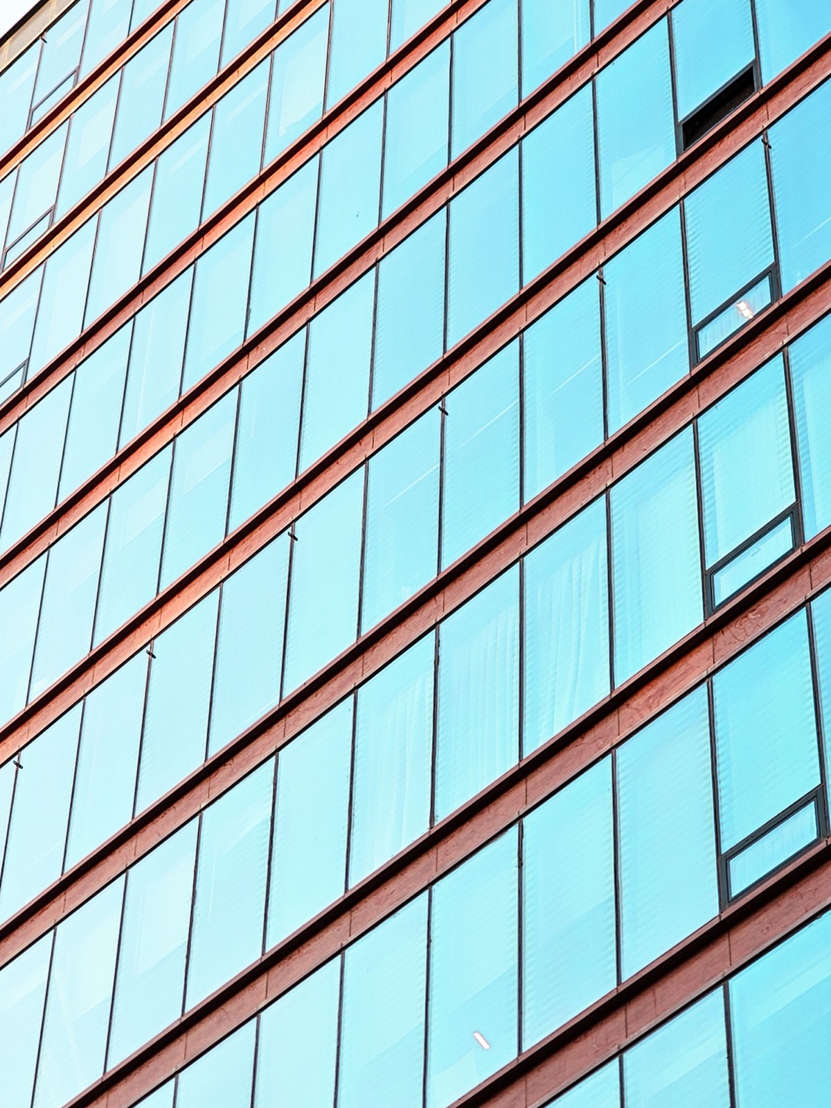 A building facade of pale blue glass panes in a regular grid, divided by warm-toned horizontal bands.